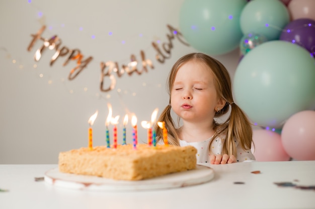 Menina bonitinha apaga velas em um bolo de aniversário em casa, num contexto de balões. aniversário da criança