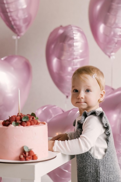 Menina bonitinha bebê de 1º aniversário com balões de coração rosa e bolo de aniversário