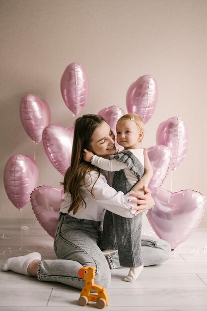 Menina bonitinha bebê de 1º aniversário com mãe e zona de foto de balão de corações de balão rosa