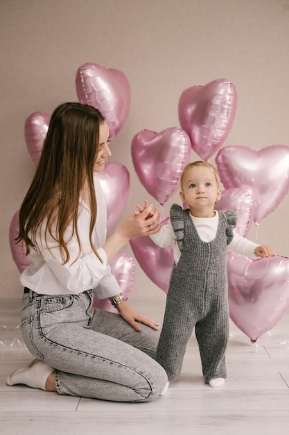 Menina bonitinha bebê de 1º aniversário com mãe e zona de foto de balão de corações de balão rosa