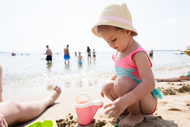 Menina bonitinha brincando com areia na praia no dia de verão