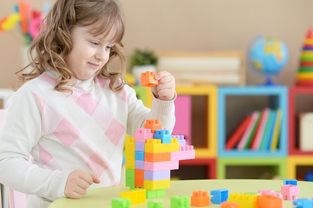 Menina bonitinha brincando com blocos de plástico coloridos no quarto