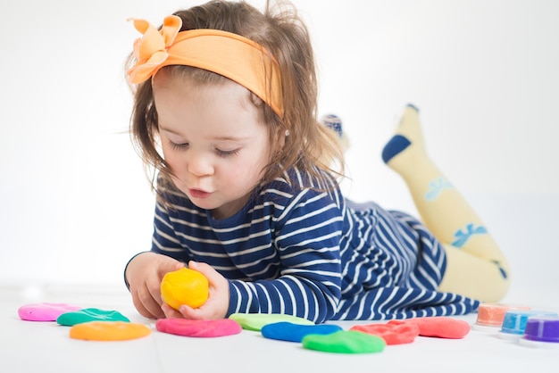 Menina bonitinha brincando com plasticina colorida em um fundo branco