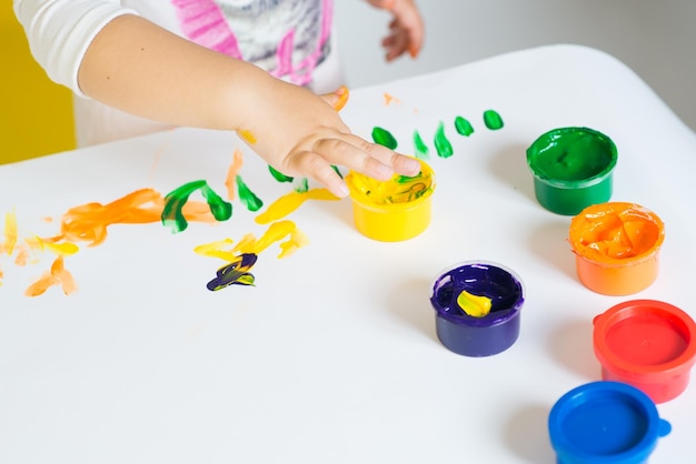 Menina bonitinha brincando com tintas coloridas em um fundo branco