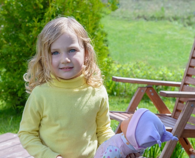 Menina bonitinha brincando com uma boneca no jardim.