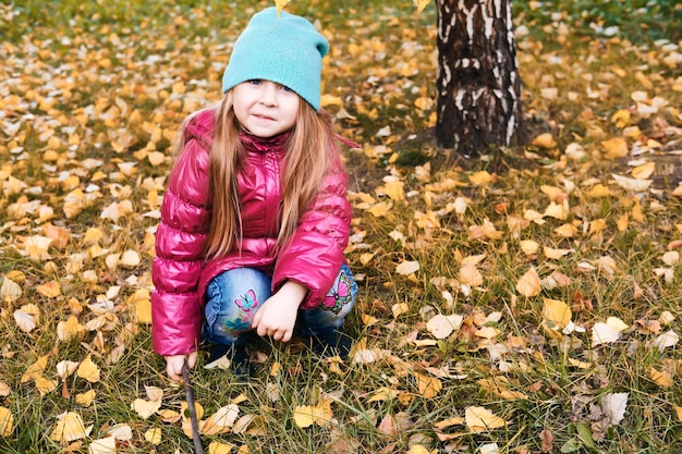 Menina bonitinha caminha no parque e brinca com folhas de outono