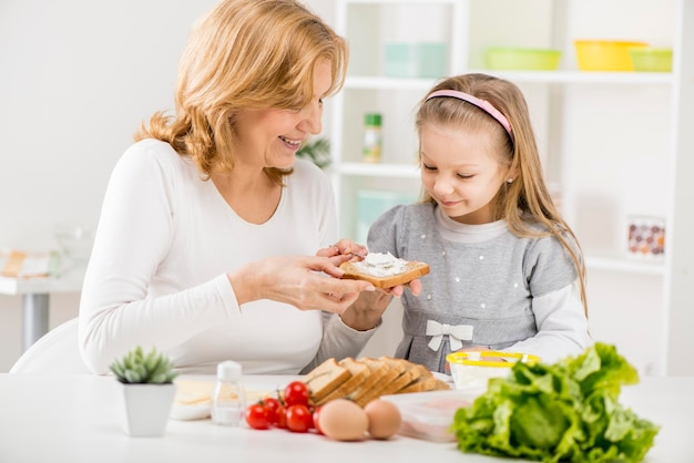 Menina bonitinha com a avó fazendo um sanduíche na cozinha.