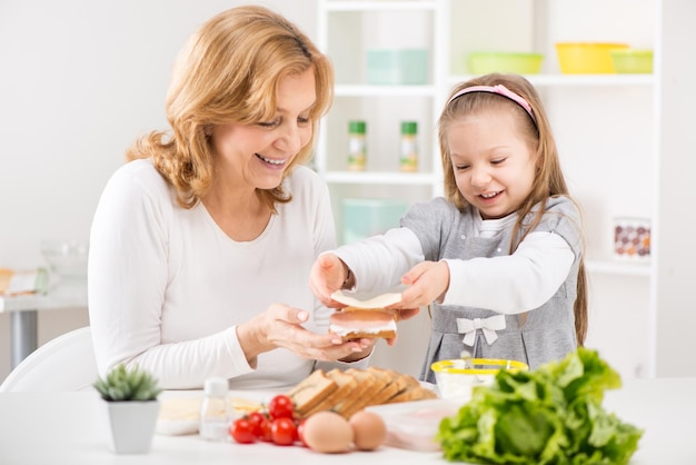 Menina bonitinha com a avó fazendo um sanduíche na cozinha.