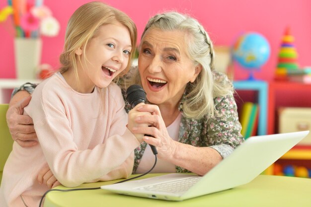 Menina bonitinha com a avó usando laptop moderno cantando karaokê