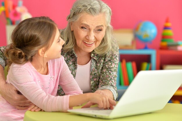 Menina bonitinha com a avó usando laptop moderno