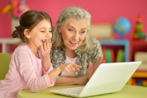 Menina bonitinha com a avó usando laptop moderno