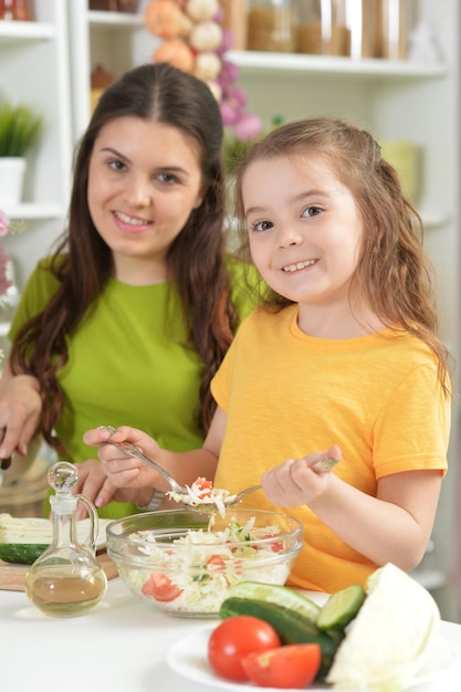 Menina bonitinha com a mãe cozinhando juntos na mesa da cozinha