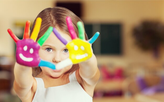 Menina bonitinha com as mãos pintadas de cores sobre fundo azul