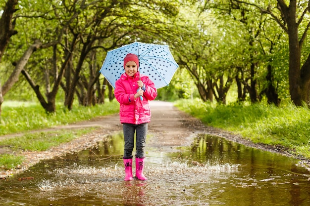 menina bonitinha com botas de chuva pulando em uma poça