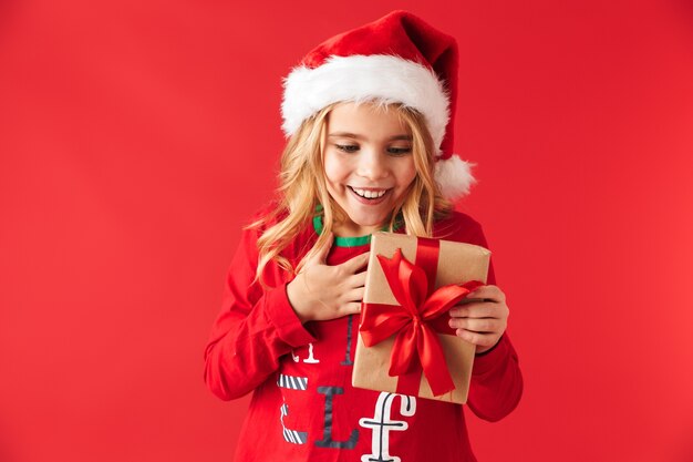 Menina bonitinha com chapéu de Natal isolada, segurando uma caixa de presente