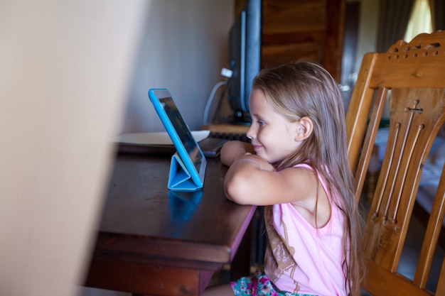 Menina bonitinha com computador tablet dentro de casa