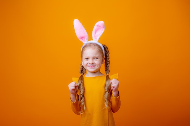 Menina bonitinha com orelhas de coelhinho da Páscoa em um fundo amarelo mostra diferentes emoções, alegria sonhando