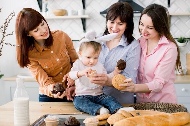 Menina bonitinha com orelhas de coelho na cabeça e sua linda mãe, tia e avó estão comendo cupcakes que eles têm nas mãos. Feriados da Páscoa ou dia das mães