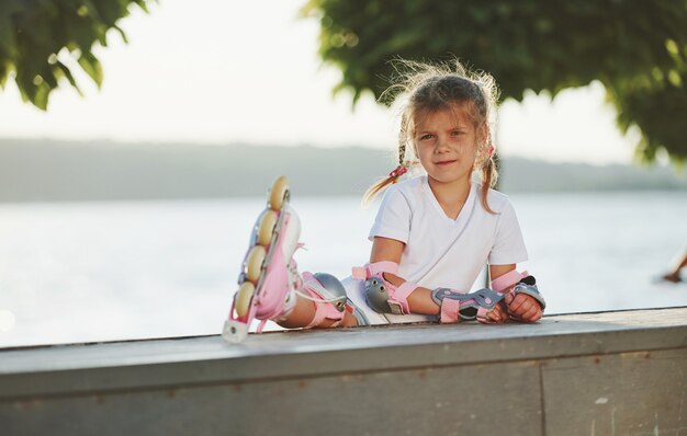 Menina bonitinha com patins ao ar livre senta-se na rampa para esportes radicais.