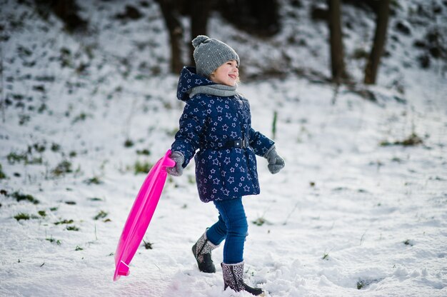 Menina bonitinha com pires trenós ao ar livre em dia de inverno.