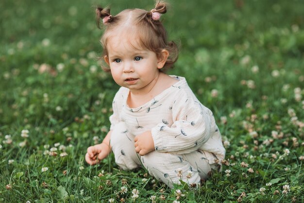 menina bonitinha com um penteado engraçado está sentado em um gramado verde florescente no parque Estilo de vida