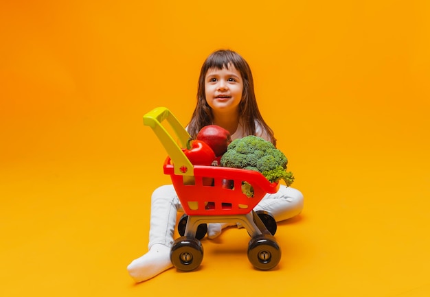 Menina bonitinha com uma cesta de mantimentos de um supermercado isolado em um fundo amarelofoto de estúdio