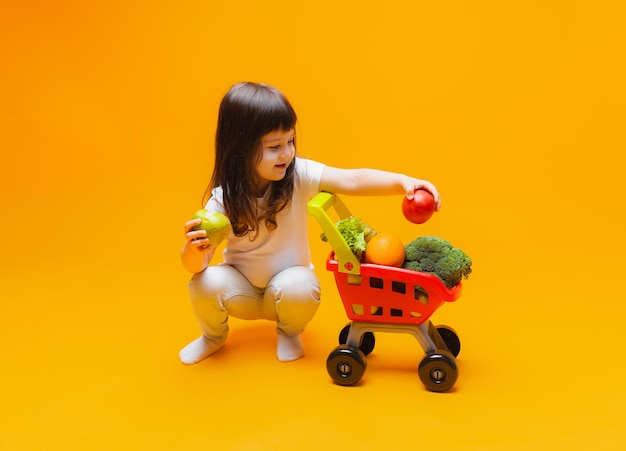 Menina bonitinha com uma cesta de mantimentos de um supermercado isolado em um fundo amarelofoto de estúdio