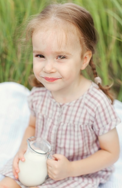 Menina bonitinha com uma jarra de leite no campo num dia de verão, infância feliz.