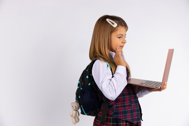 Menina bonitinha com uniforme escolar, segurando um computador laptop mostrando Olá isolado na parede cinza. Conceito de aprendizagem online.