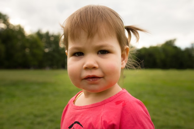 Menina bonitinha com vestido rosa brincando no parque em frente à grama verde