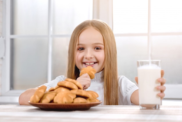 Menina bonitinha come biscoito com leite e sorrindo