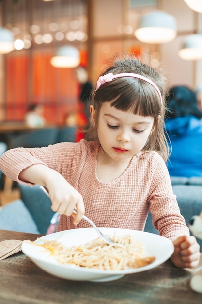 Menina bonitinha comendo espaguete com molho sentado em um restaurante