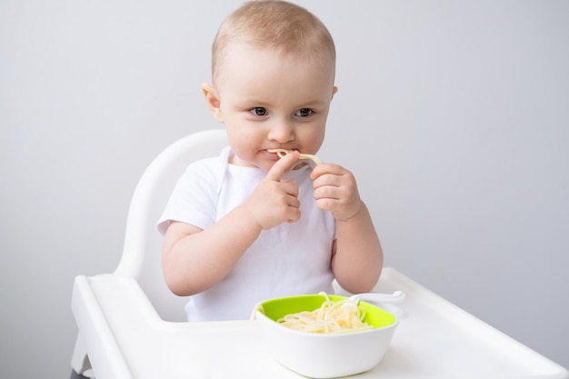 menina bonitinha comendo macarrão espaguete sentado na cadeira de bebê na cozinha branca