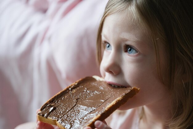 Menina bonitinha comendo pão com macarrão de chocolate por cima, doces saborosos