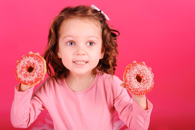 Menina bonitinha comendo rosquinhas doces sobre fundo rosa