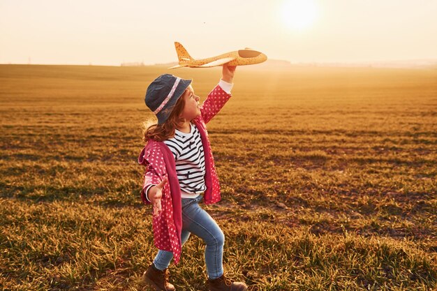 Menina bonitinha corre com avião de brinquedo no belo campo no dia ensolarado