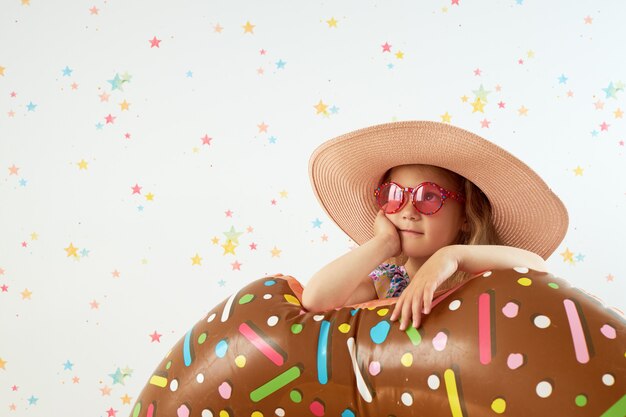 Menina bonitinha criança de chapéu com anel inflável na parede de cor. quarentena de férias de verão em casa