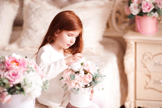 Menina bonitinha de 3 a 4 anos segurando flores sentadas na sala perto da primavera Infância