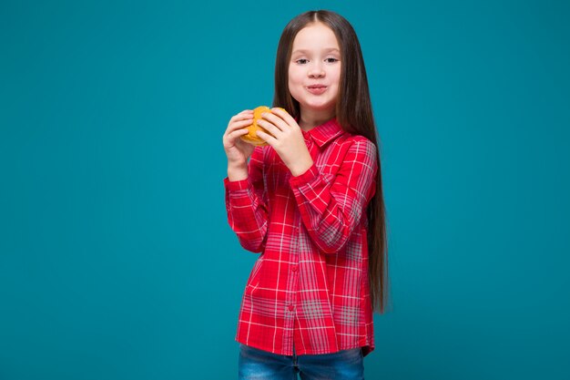 Menina bonitinha de camisa quadriculada com cabelo moreno segurar hambúrguer