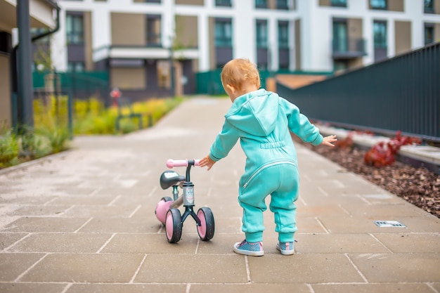 Menina bonitinha de macacão azul andando na bicicleta de equilíbrio de corrida feliz saudável adorável bebê criança ...