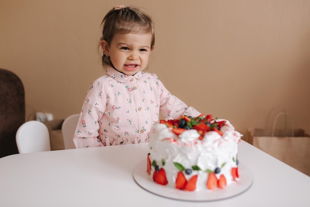 Menina bonitinha de um ano e meio esperando delicioso bolo de aniversário Menina de dezoito meses muito feliz e rindo Comida vegetariana Sem lactose e sem glúten