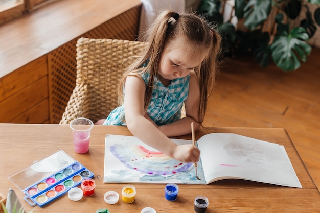 Menina bonitinha desenha com um pincel e pinta na mesa da sala de estar