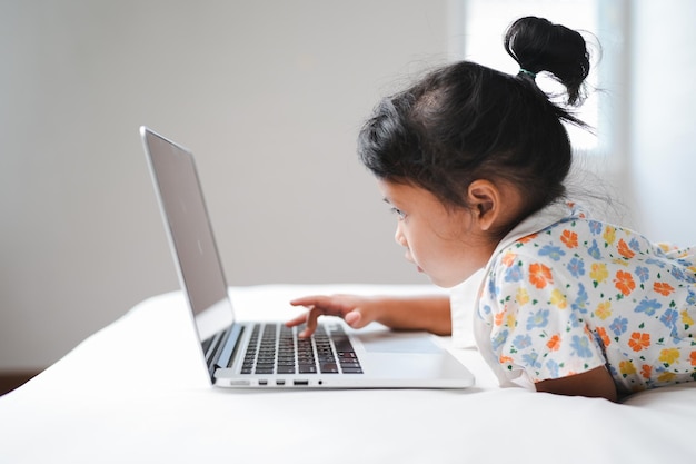 Menina bonitinha digitando no teclado do notebook aprendendo online escola em casa