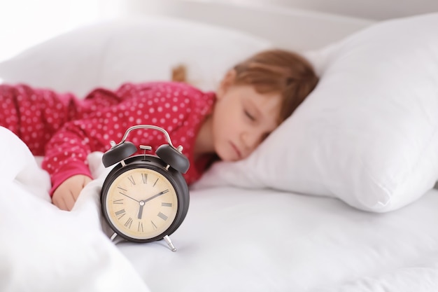 Foto menina bonitinha dormindo na cama com despertador