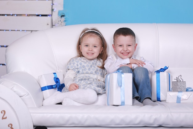 Menina bonitinha e menino com caixas de presente, sentado em um sofá branco. celebrando o Natal e o Ano Novo.