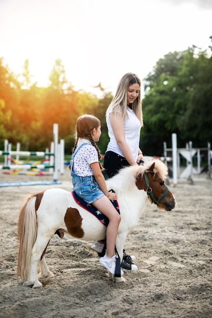 Menina bonitinha e sua irmã mais velha curtindo com um cavalo pônei ao ar livre no rancho