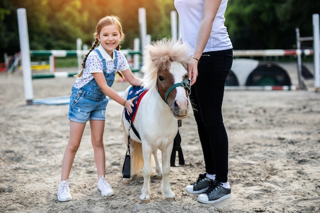 Menina bonitinha e sua irmã mais velha curtindo com um cavalo pônei ao ar livre no rancho