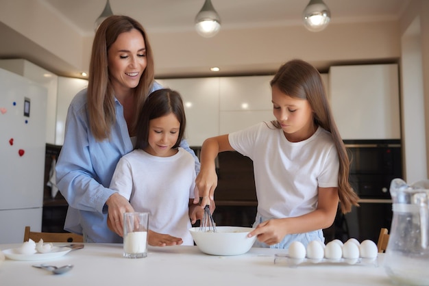 Menina bonitinha e sua linda mãe em aventais estão brincando e rindo enquanto amassando a massa na cozinha