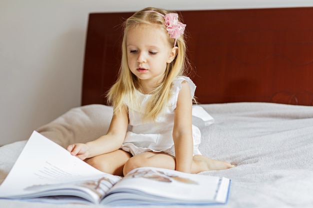 Foto menina bonitinha em elegante vestido branco, lendo um livro