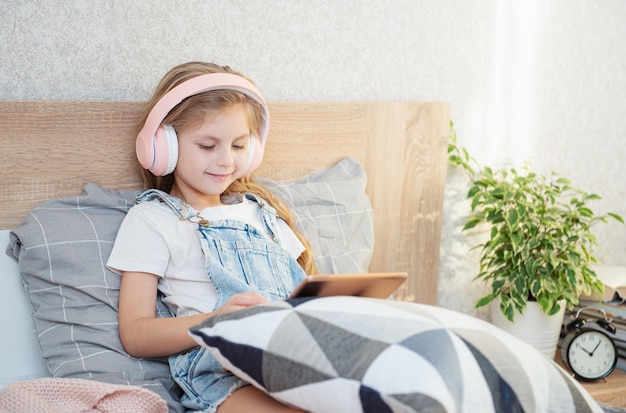 Menina bonitinha em fones de ouvido está usando um tablet em casa